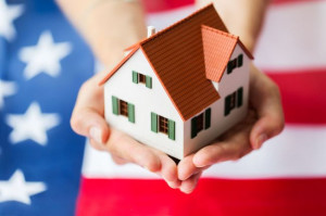 close up of hands holding house over american flag